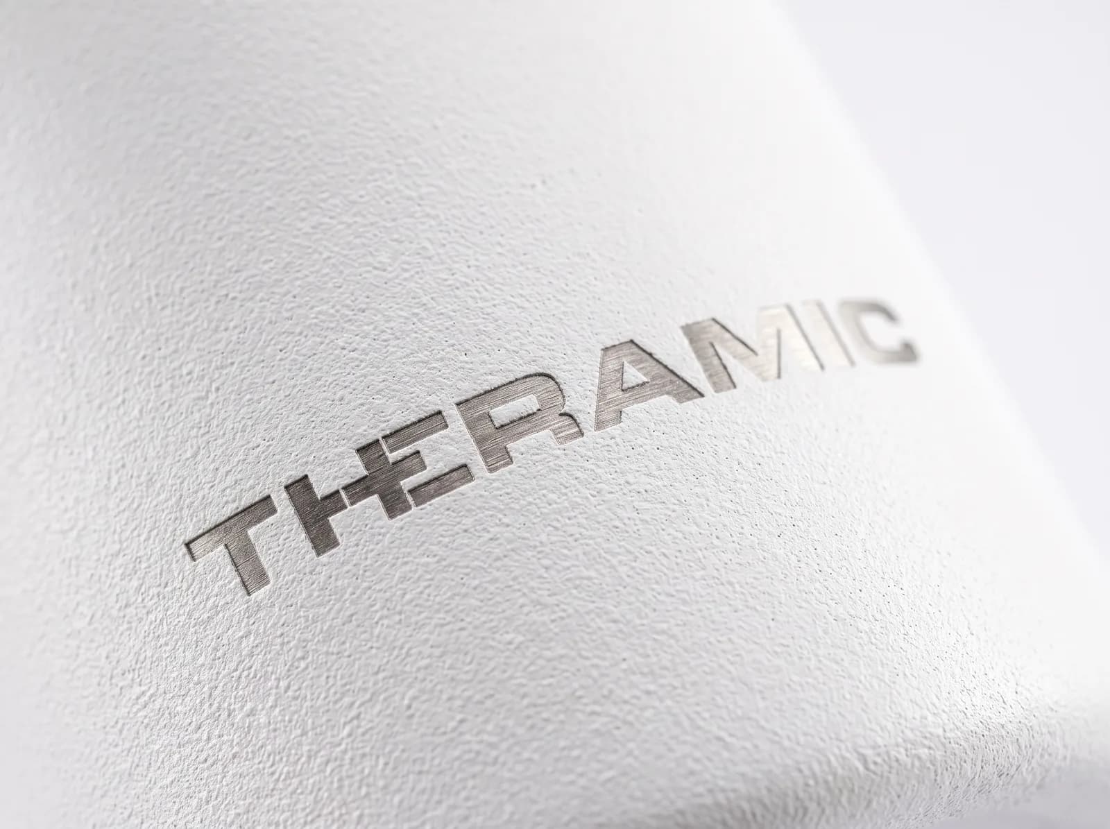 Grabado láser en una botella de acero, a contraluz: el borde del trazo del logo THERAMIC sobre el acabado mate